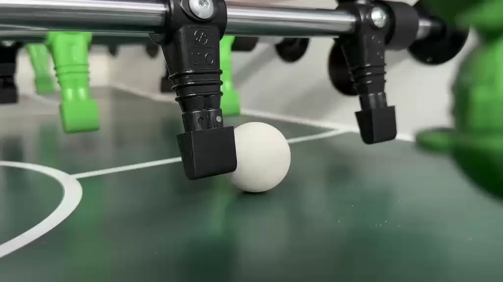 Weißer Kickerball zwischen schwarzen und grünen Tischfußballfiguren